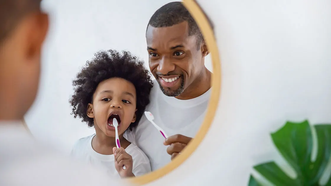 A parent and child brushing their teeth together.
